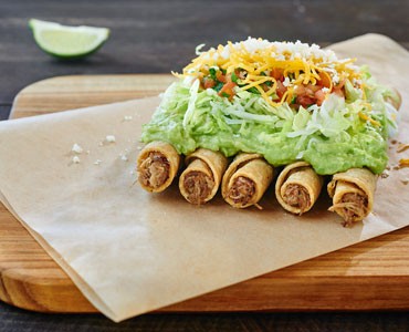 Rolled Tacos filled with Meat Covered with Guacamole and Cheese